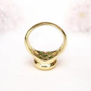 A gold ring with a green gemstone in the center, placed on a white surface.